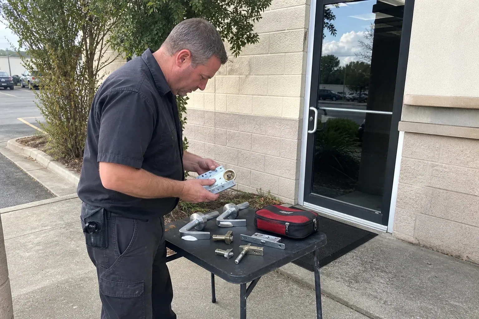 Technician examining detached commercial lock hardware on a table outside a shop entrance. — Business Lockout Service, Wasaga Beach
