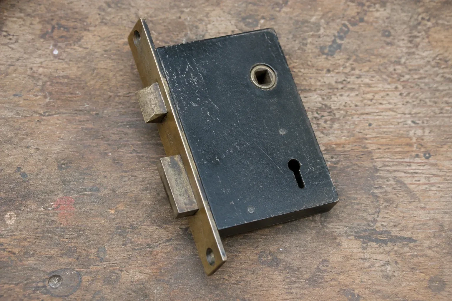 Closed mortise lock case with spindle opening, keyhole, latch and deadbolt on a wooden workbench. — Vintage Mortise Lock Service, Wasaga Beach