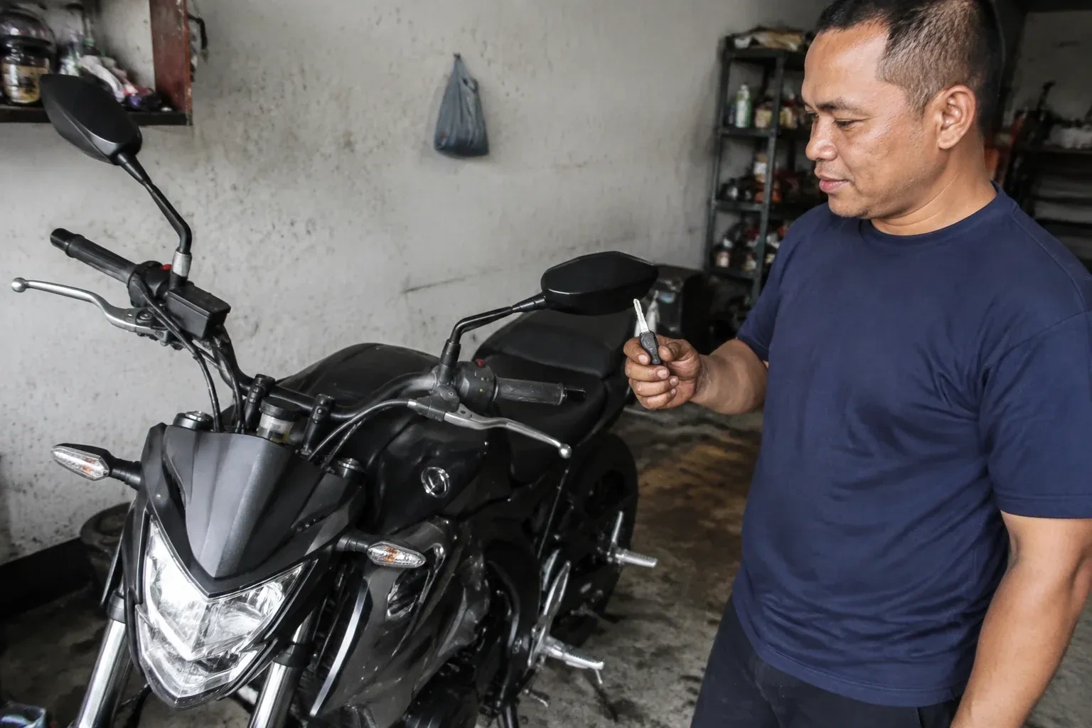 Person holding a key beside a black motorcycle in a garage. — Motorcycle & Scooter Keys, Wasaga Beach